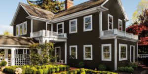 A charming two-story home with dark siding and white trim sits peacefully beneath a clear sky.