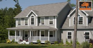 A charming gray two-story home with a welcoming porch sits peacefully amid trees and green lawn.