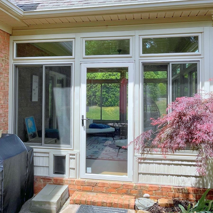 Sunlight floods through patio doors into a welcoming sunroom, with greenery and cozy outdoor touches nearby.