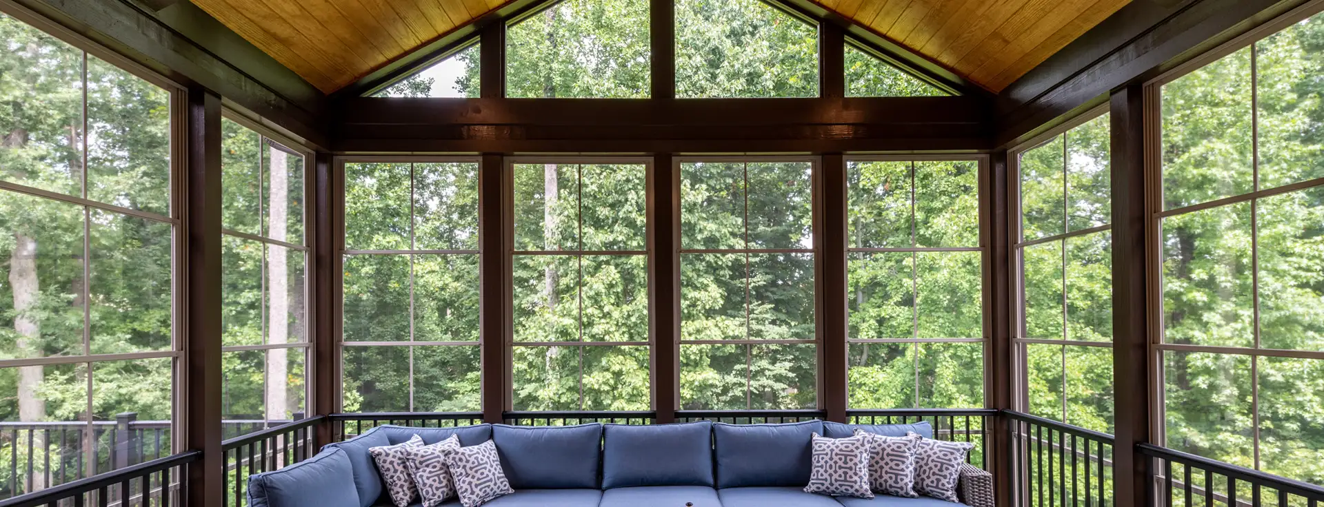 A cozy blue sectional invites relaxation beneath a vaulted wooden ceiling, surrounded by tranquil forest views.