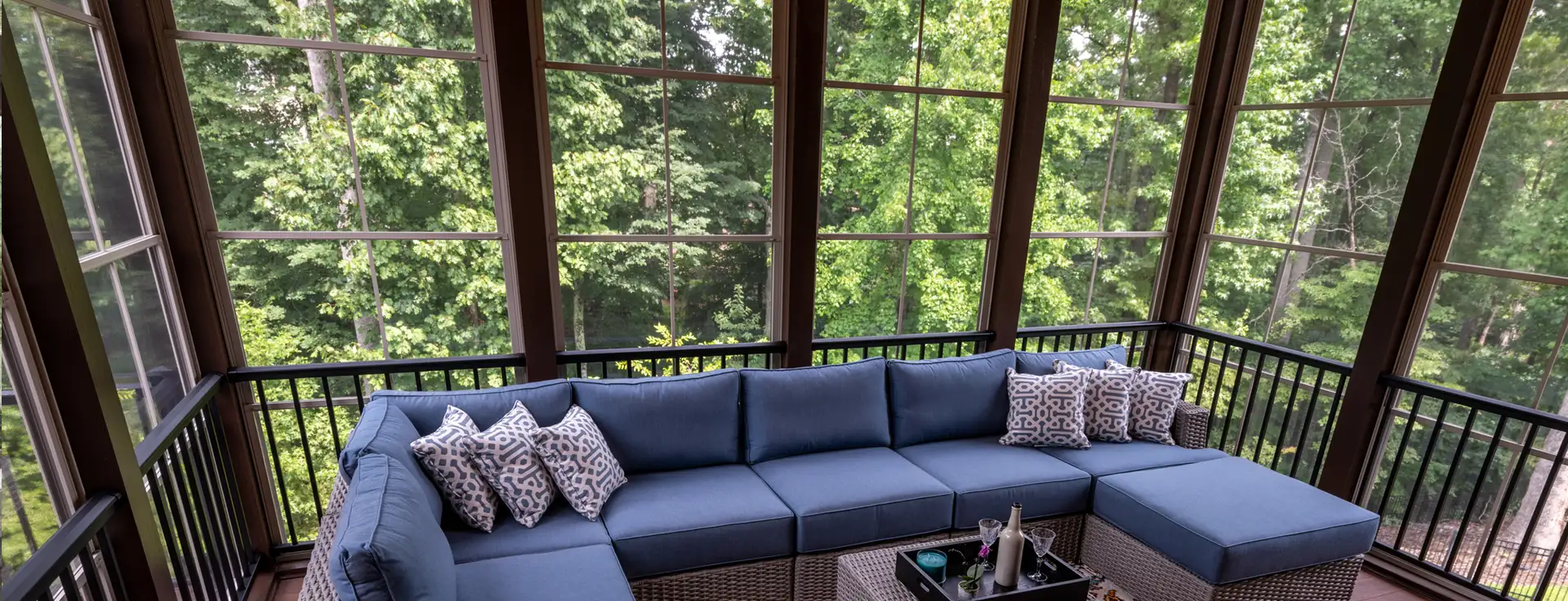 A cozy blue sectional invites relaxation on a bright screened porch overlooking lush green trees.
