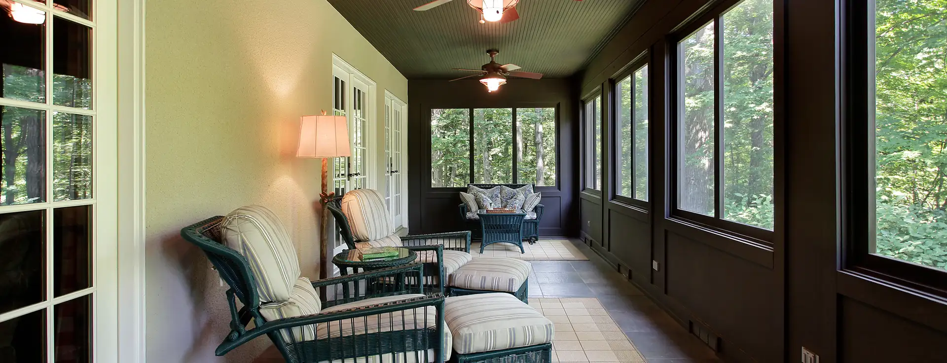 A cozy screened porch offers serene tree views through large windows in a comfortable, airy setting.