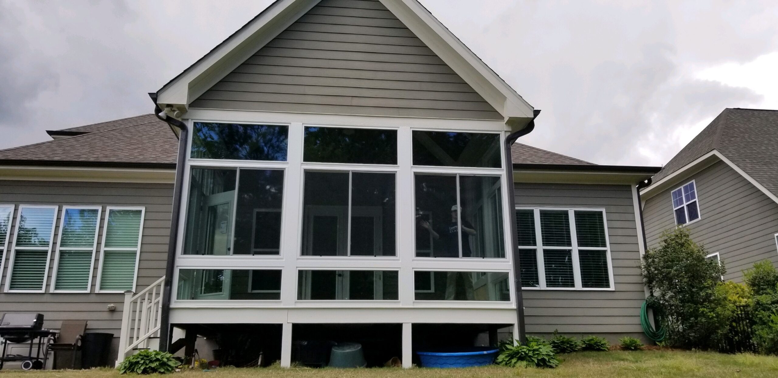 A sleek gray house features a bright, glass-walled sunroom overlooking the peaceful backyard.