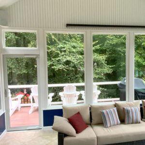 A bright sunroom with cozy seating opens to a deck nestled among trees, evoking relaxing comfort.