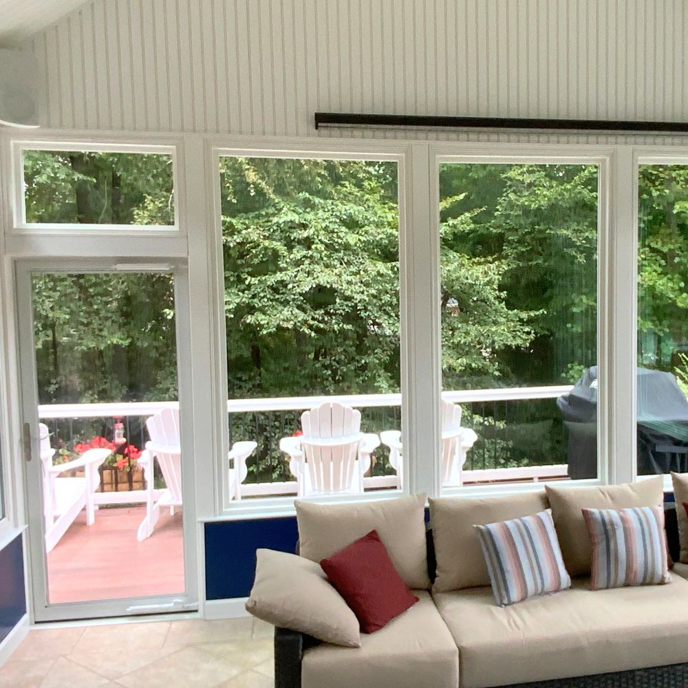 A bright sunroom with cozy seating opens to a deck nestled among trees, evoking relaxing comfort.