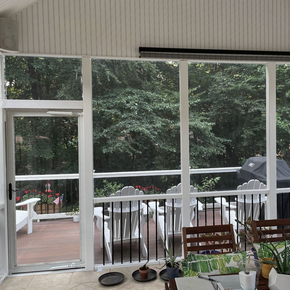A bright screened porch with white windows creates an inviting, tranquil retreat overlooking a peaceful deck.