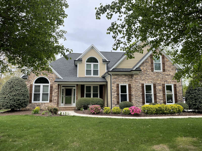 A welcoming suburban home stands amid lush greenery and blooming bushes, exuding warmth and charm.