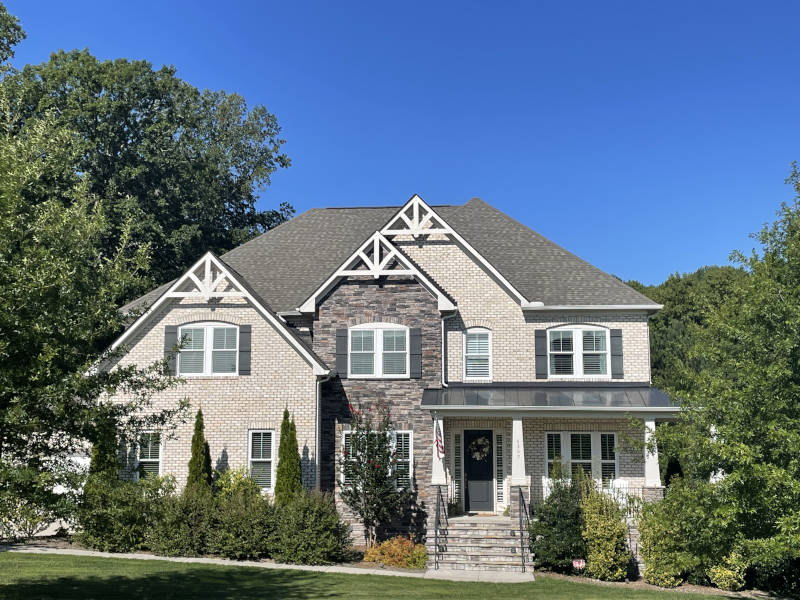 A charming two-story suburban home nestles amid lush greenery beneath a bright blue sky.