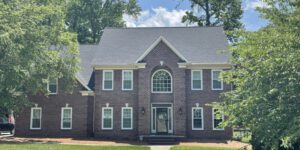 A stately brick house stands amid lush greenery, sunlight illuminating its grand arched window.