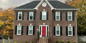 A stately red brick house stands amid autumn trees, exuding warmth with its bold door and elegant windows.