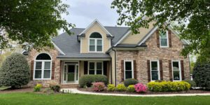 A charming suburban house stands amidst lush greenery and flowers beneath graceful overhanging tree branches.