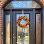 A black door with glass panels and an autumn wreath welcomes visitors to this elegant brick home.