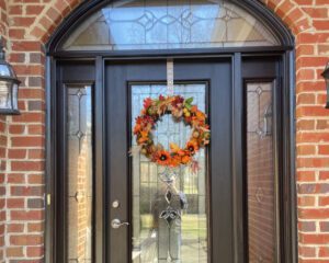 A black door with glass panels and an autumn wreath welcomes visitors to this elegant brick home.