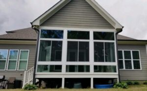 A gray house with a bright, airy raised sunroom radiates tranquility amid simple greenery.