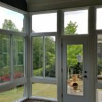 A bright sunroom with expansive windows offers peaceful views of a lush yard and trees.