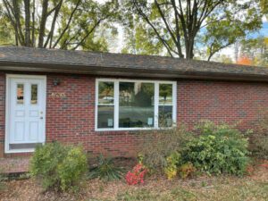A cozy brick house nestles amid greenery, fallen leaves hinting at a tranquil autumn setting.