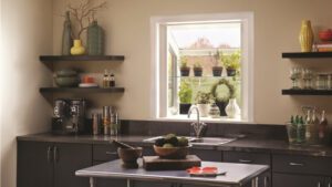 A sleek black-cabinet kitchen feels airy and bright, framed by lush garden views through the window.
