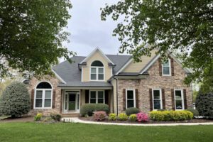 A charming single-story house sits amid blooming gardens, elegantly framed by leafy trees.