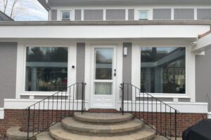 A welcoming gray house features a white door framed by new windows and elegant brick steps.