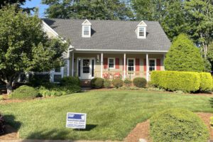 A charming gray house with red shutters and a lush lawn features a Window Depot sign out front.