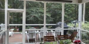 A cozy screened porch overlooks a tranquil, tree-lined deck, inviting relaxation in a serene setting.