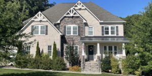 A charming brick house with stone accents sits serenely among greenery beneath a clear blue sky.