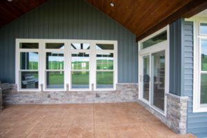 A welcoming covered patio features elegant stamped concrete and large glass doors against blue siding with stone accents.