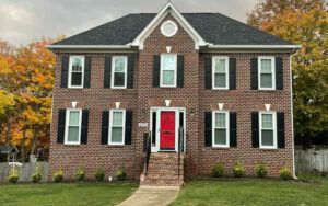 A charming brick house with a red door nestles among autumn trees, creating an inviting atmosphere.