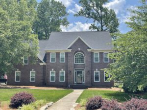 A stately brick house stands serenely amid a manicured yard beneath a partly cloudy sky.