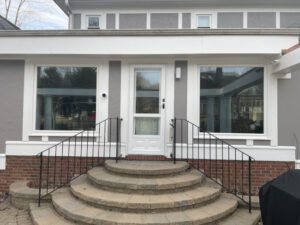 A modern gray house features a welcoming white door framed by large windows and elegant brick steps.